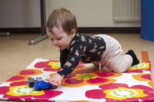Pieni lapsi leikkii lattialla muoviautolla