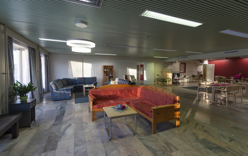Kuva Osallisuuskeskus Ainolan Olohuone-tilasta. Etualalla punainen sohva ja sohvapöytä. Taka-alalla sininen sohvaryhmä sekä pöytiä ja penkkejä.