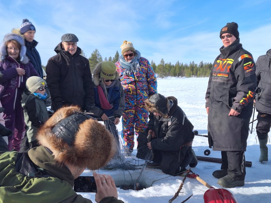 Leiriläiset järven jäällä kokemassa juomuksia, eli talvikalastusverkkoja